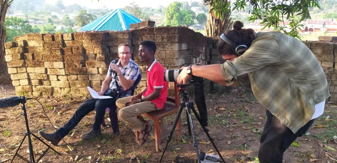 Documentary camera operator filming an outdoor interview with two participants